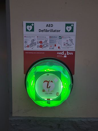 Öffentlicher AED neben dem Nebeneingang an der Gebäuderückseite