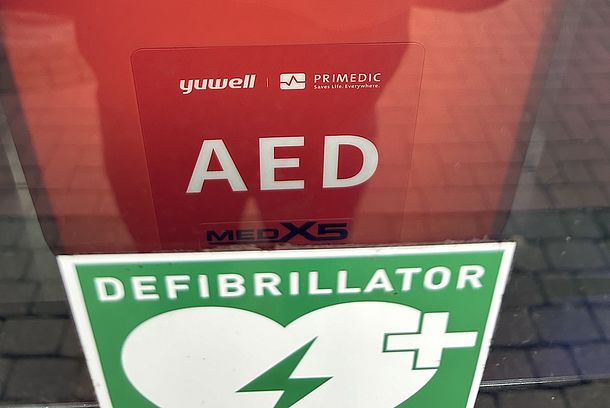 AED im silbergrauen Wandkasten neben dem Eingang