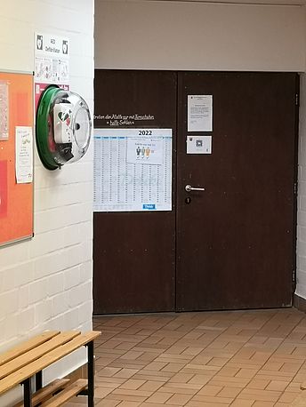 Um die Ecke, schräg gegenüber dem Eingang zur Sporthalle AED im Wandkasten Um die Ecke, schräg gegenüber dem Eingang zur Sporthalle AED im Wandkasten